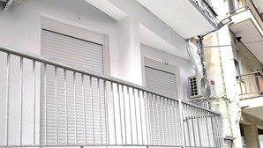 Een balkon met een metalen hekwerk en gesloten luiken, een witte muur en een airconditioner.