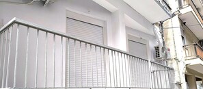 Ein Balkon mit Metallgeländer und geschlossenen Fensterläden, eine weiße Wand und eine Klimaanlage.