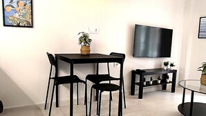 Een moderne woonkamer met een eettafel, stoelen, een flatscreen televisie en een potplant.