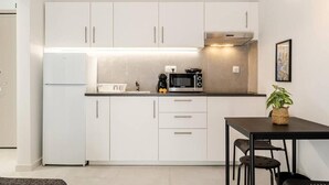 Een kleine keuken met witte kastjes, een magnetron, een kookplaat en een eethoek met een tafel en stoelen.
