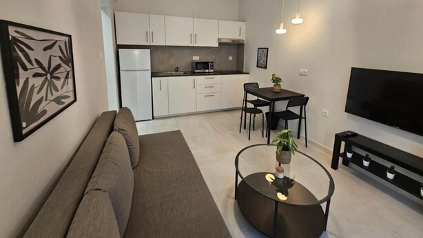 Een moderne woonkamer met een bank, salontafel, televisie en een eethoek met stoelen en een tafel.