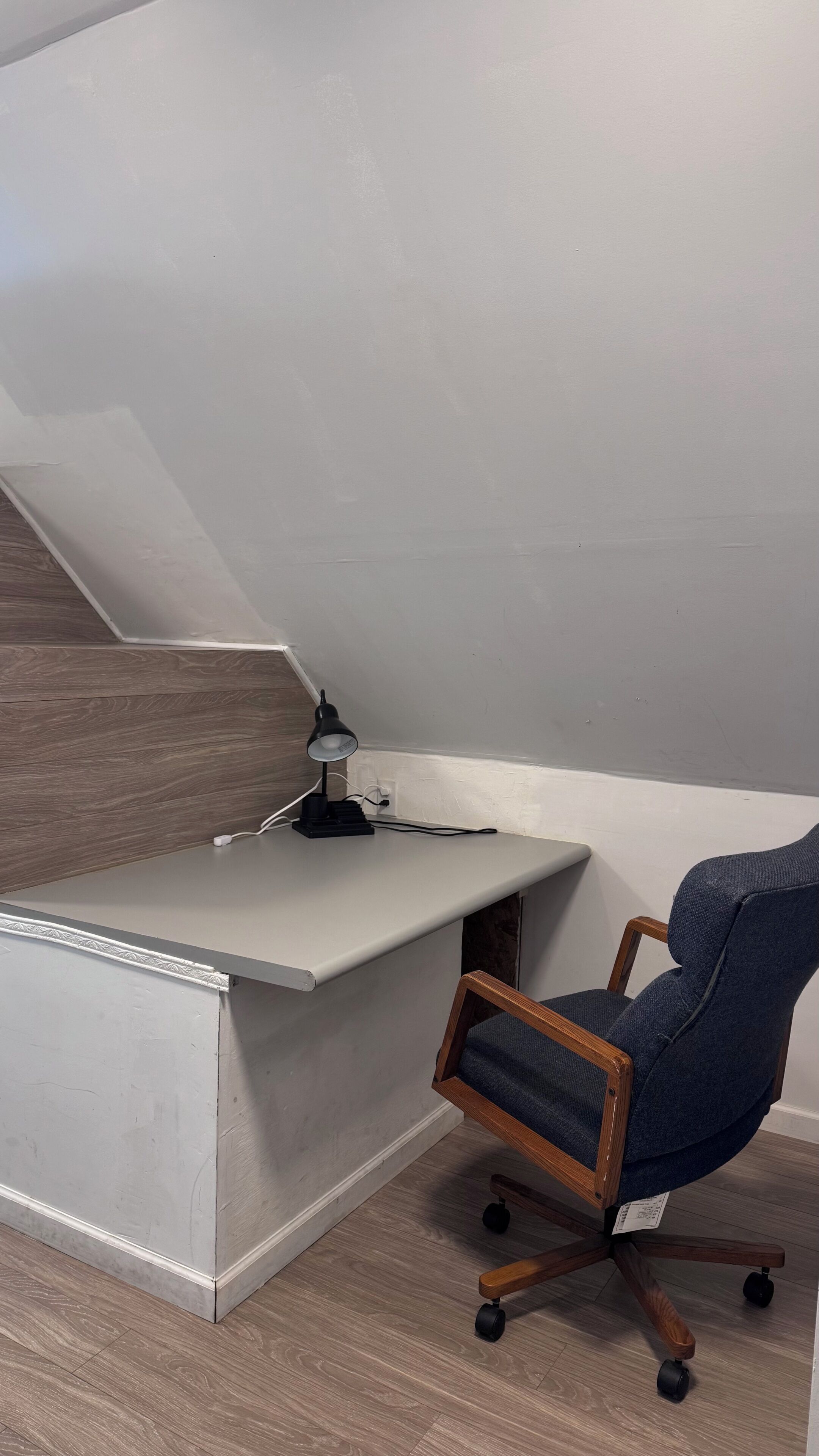 Escritorio en esquina con silla, lámpara y piso de madera.