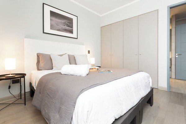 A modern bedroom with a bed, bedside tables, a wardrobe, and a framed picture on the wall. - Departamento 4 Pax Barrio Italia (Santiago)