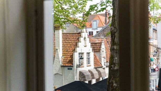 A view through a window of a street with buildings, a tree, and a black umbrella. - Amazing scenic city view room The Lake Suites (Brugge)