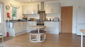 A modern kitchen with white cabinets, a round table, and a built-in oven. - Bright 2-Bed Cottage in South Skye |Dog-Friendly Retreat Near Coast & Distillery (Bristol)