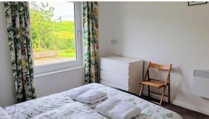 Um quarto com uma cama, uma cadeira, uma cômoda e uma janela com cortinas.