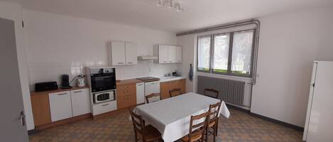 Une cuisine compacte comprenant une table à manger, des chaises, un réfrigérateur et une fenêtre avec des rideaux.