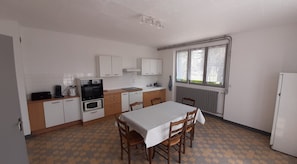 A compact kitchen with a dining table, chairs, a refrigerator, and a window with curtains. - Le Gîte de Corcelles – Spacious Ground Floor Apartment with Terrace and Parking (Arlay)