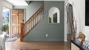 Un salon avec un escalier en bois, un grand miroir et une plante en pot.