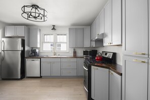 A modern kitchen with grey cabinets, stainless steel appliances, and a wooden countertop. - Charles Cottage Near Warren St New Renovation (Hudson)