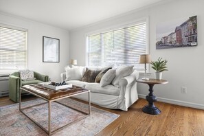 A living room with a white sofa, a green armchair, a coffee table, and a side table with a lamp and plant. - Charles Cottage Near Warren St New Renovation (Hudson)