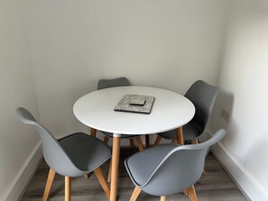A round table with four grey chairs, a white tablecloth, and a small book or folder on the table. - Carmen Sylva Llandudno Beach Family  Flat (Llandudno)