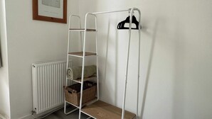 En vit hylla i metall med korgar och en svart klädhängare, placerad mot en vägg med en inramad tavla.
