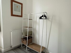 Ein weißes Metallregal mit Körben und einem schwarzen Kleiderhaken vor einer Wand mit einem gerahmten Bild.