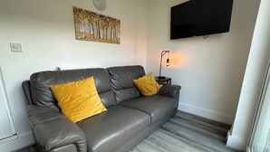 Ett modernt vardagsrum med en soffa i läder, två kuddar i senapsgul färg, en platt-TV som är monterad på väggen och en golvlampa.