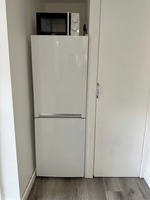 Ein weißer Kühlschrank mit Mikrowelle obenauf, einer Türgriff und ein Holzboden.
