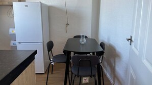 Una cocina compacta con un refrigerador blanco, una mesa de comedor con cuatro sillas y una pequeña encimera.