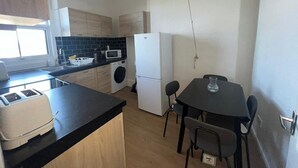 Cocina compacta equipada con lavadora, microondas, refrigerador, tostadora y una mesa de comedor con sillas.