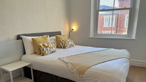Un dormitorio con cama, mesita de noche y ventana.