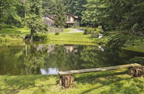 A serene lakeside setting with a wooden bench, a rustic house, and lush greenery. - Hudson Valley Private Retreat with 3 bedrooms, 2 living spaces, and a pond. (Hillsdale)