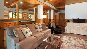 A cozy living room with a sofa, armchair, and coffee table, wooden beams on the ceiling, and a view of the kitchen area. - Hudson Valley Private Retreat with 3 bedrooms, 2 living spaces, and a pond. (Hillsdale)