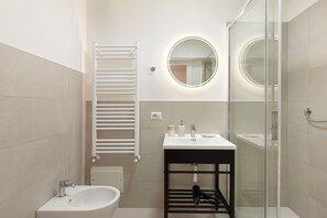 A modern bathroom with a bidet, a glass shower enclosure, and a white sink with a mirror. - Pharmacy B (stresa)