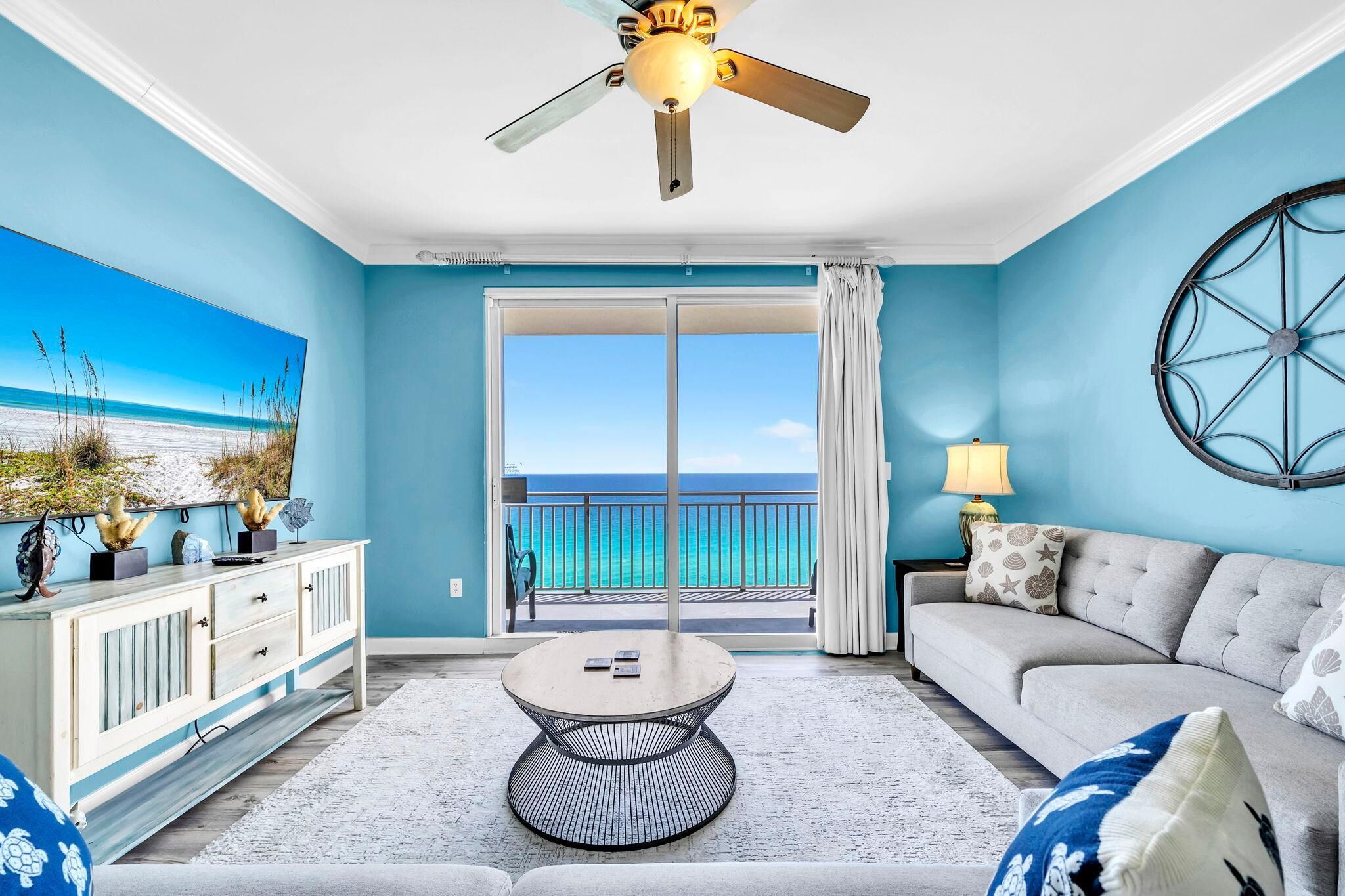 A room with a ceiling fan, a sofa, a coffee table, a cabinet, and a view of the ocean.