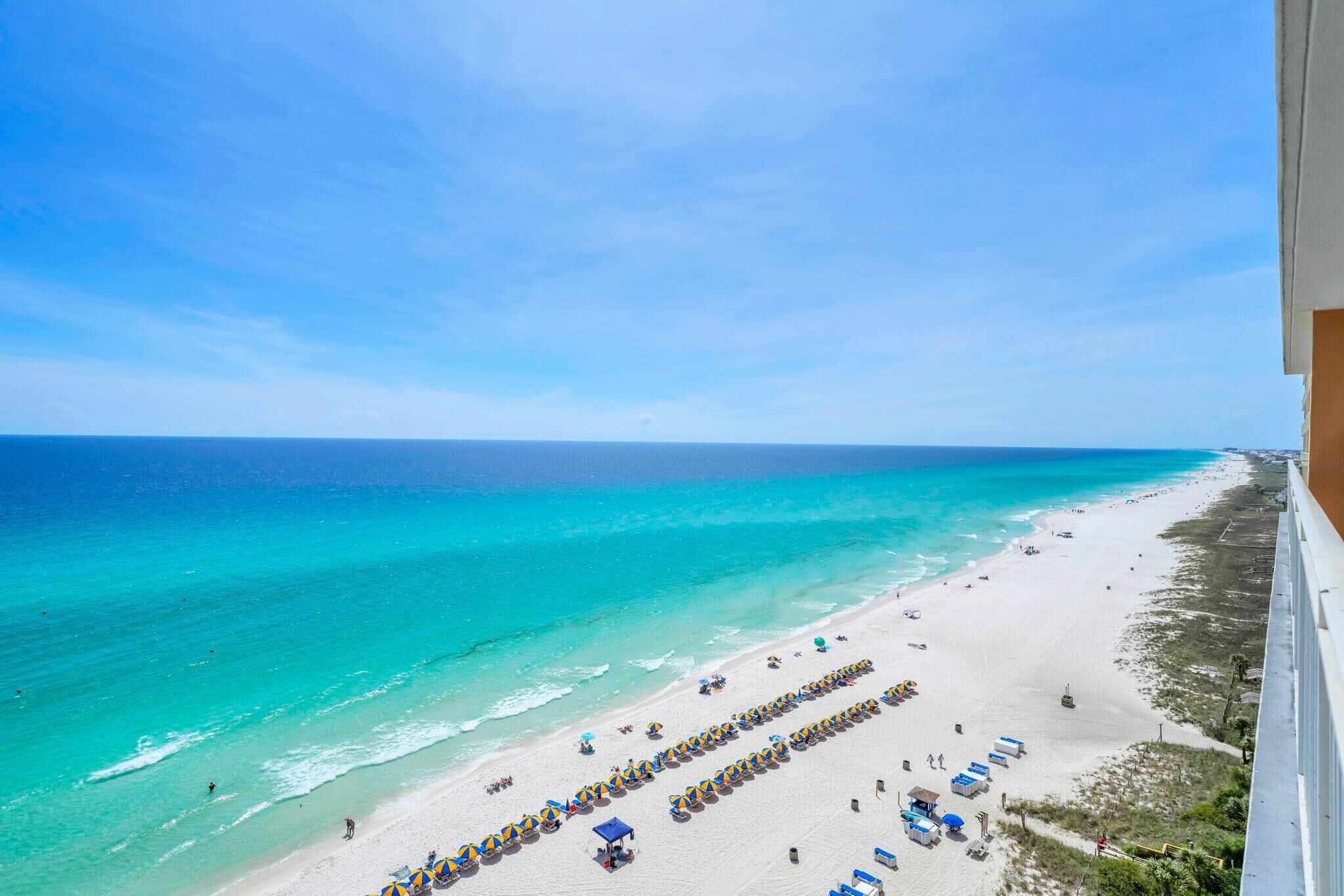 Une plage bordée de rangées de transats et de parasols, un ciel dégagé et l’océan.