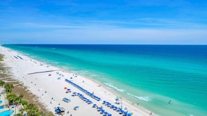 Ein Strand mit einer weiten Sandfläche, einem klaren blauen Meer und einer Reihe blauer Sonnenschirme.