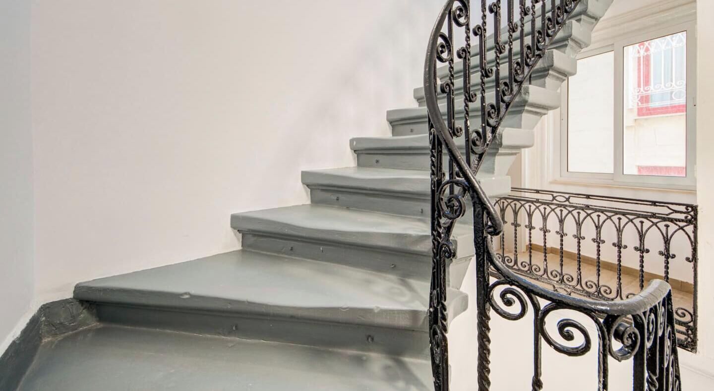 A staircase with a wrought iron railing and a window with red and white striped shutters.