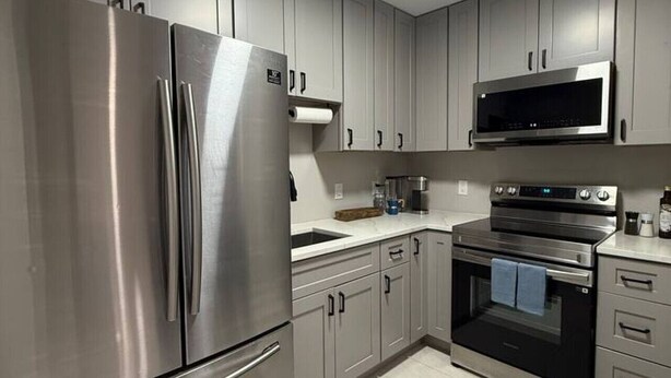 A modern kitchen with stainless steel appliances, grey cabinets, and a tiled floor. - Cozy Palm Retreat 2BR Home • Near Beaches (Lake Worth Beach)