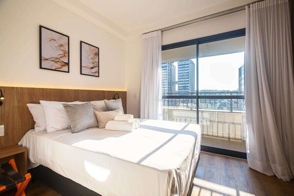 Habitación de hotel con una cama grande, vistas de edificios a través de la ventana y dos cuadros enmarcados en la pared.