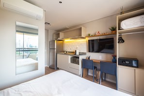 A compact hotel room with a kitchenette, a bed, a dining area, and a view of the city.