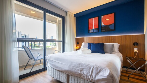 Ein Hotelzimmer mit einem großen Bett, Blick durch eine Schiebetür, einem Holzkopfbrett und einem modernen Wandbild.