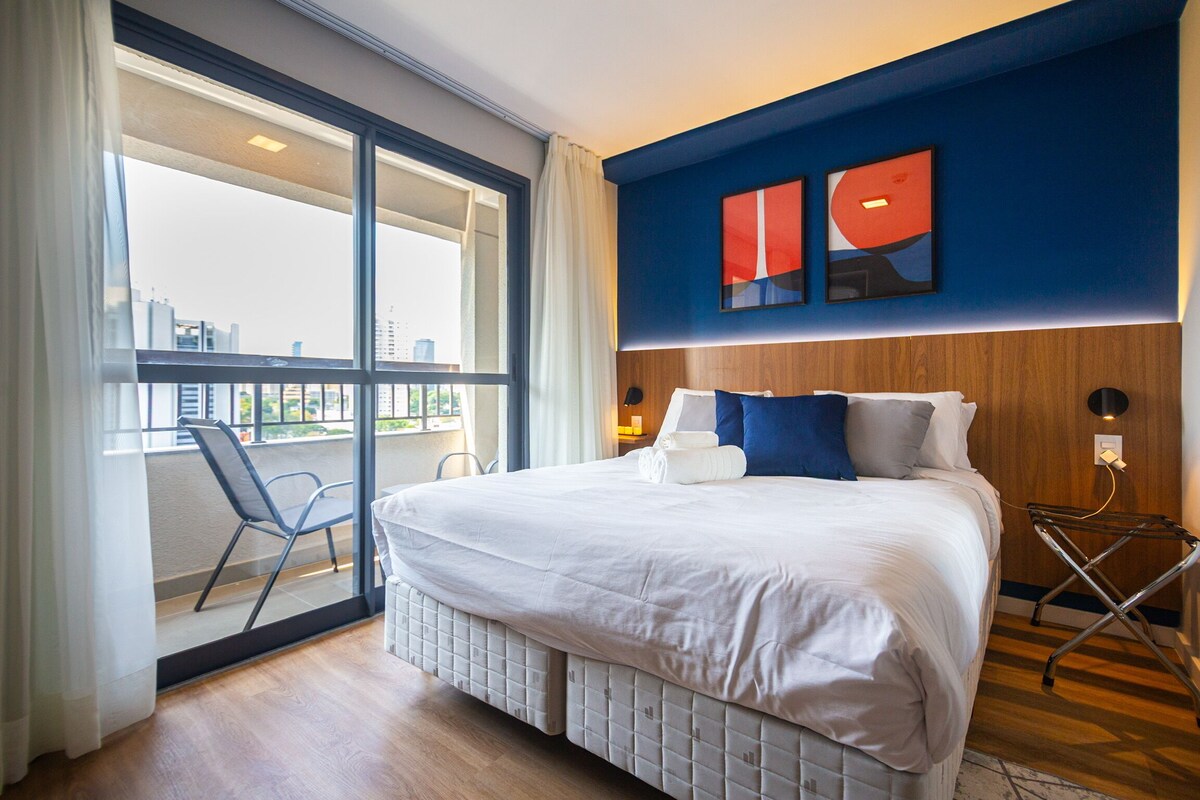 A hotel room with a large bed, a view through a sliding glass door, a wooden headboard, and a modern wall art piece.