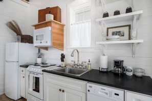 A kitchen with white cabinetry, a stove, a sink, and a dishwasher. There are shelves with cups and a framed picture.