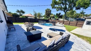 A backyard with a pool, outdoor furniture, and a fenced area.