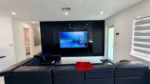 A modern living room with a large flat-screen TV, black leather sofas, and a marble-patterned floor.