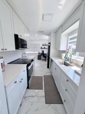 Une cuisine moderne avec des meubles blancs, une cuisinière noire, un évier et une fenêtre donnant sur un beau paysage.