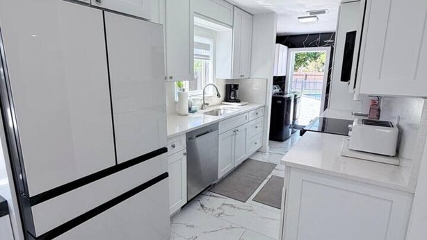 A modern kitchen with white cabinetry, a stainless steel refrigerator, a built-in oven, and a marble floor.