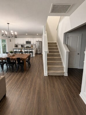 A modern kitchen with white cabinets, stainless steel appliances, and a dining area with a wooden table and chairs. - Spacious 5-bedroom house in lovely Castle Hayne, minutes to wrightsville beach (Castle Hayne)