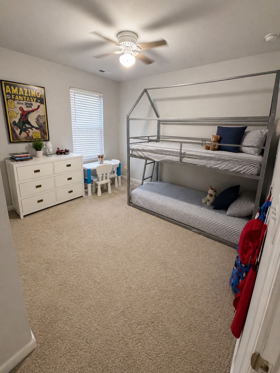 Une chambre avec des lits superposés, un bureau, une chaise, un ventilateur de plafond et une affiche accrochée au mur.