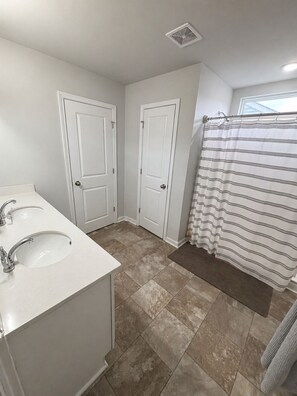 A bathroom with two white doors, a striped shower curtain, and a sink with a mirror. - Spacious 5-bedroom house in lovely Castle Hayne, minutes to wrightsville beach (Castle Hayne)