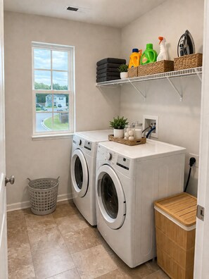 A laundry room with two front-loading washing machines, a drying rack, a basket, and shelves with cleaning supplies. - Spacious 5-bedroom house in lovely Castle Hayne, minutes to wrightsville beach (Castle Hayne)