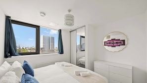 A modern hotel room with a large bed, a view of the city, and a unique wall decoration. - East India Dock Road, London (Greater London)