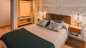 Ein Schlafzimmer mit Steinwand, Holz-Kopfteil, einem Bett mit gemusterten Kissen, einem Kleiderschrank und Nachttischlampen.