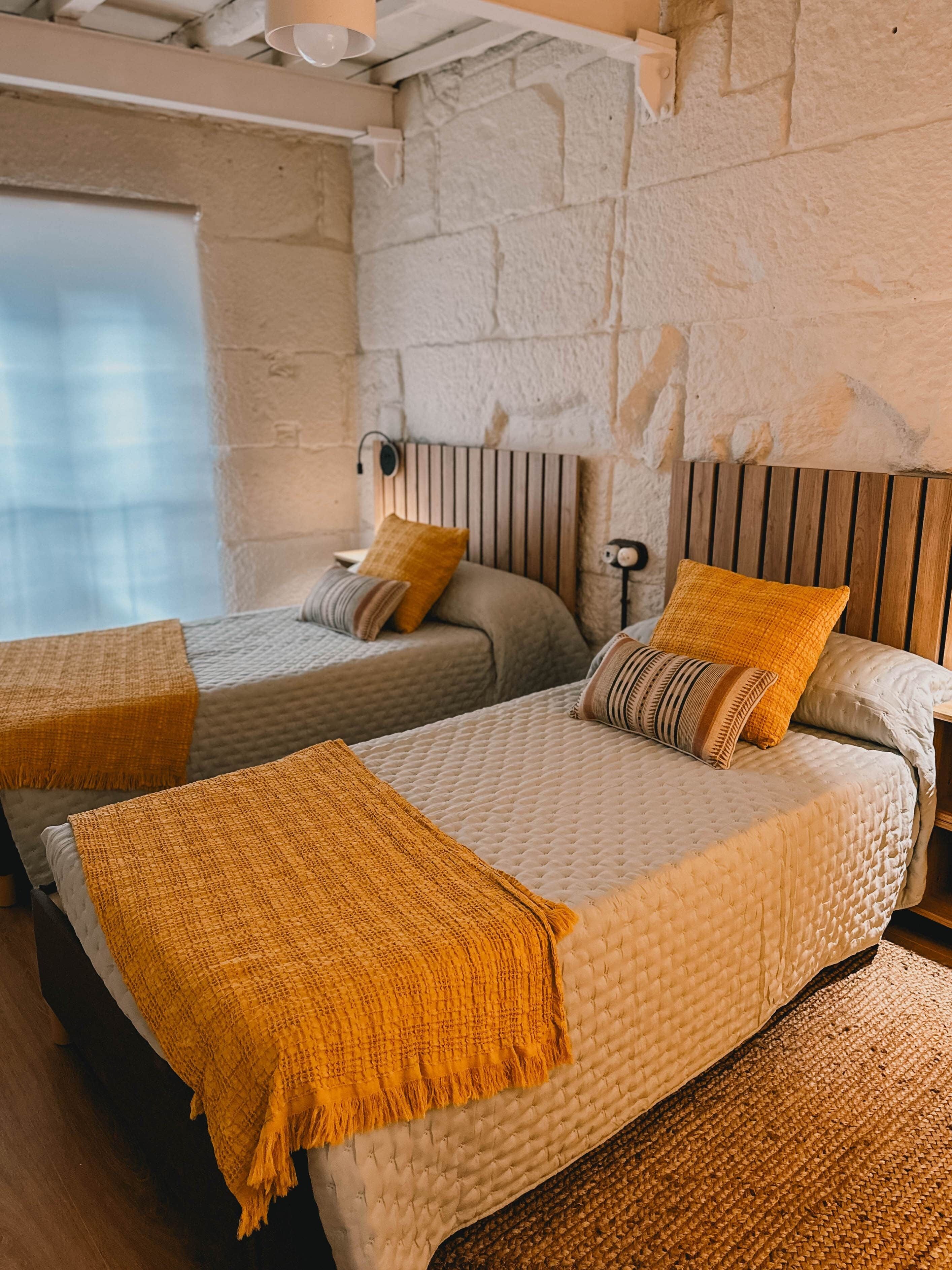 Une chambre avec deux lits, chacun doté d’une tête de lit, d’une fenêtre et d’un mur à la texture pierre.