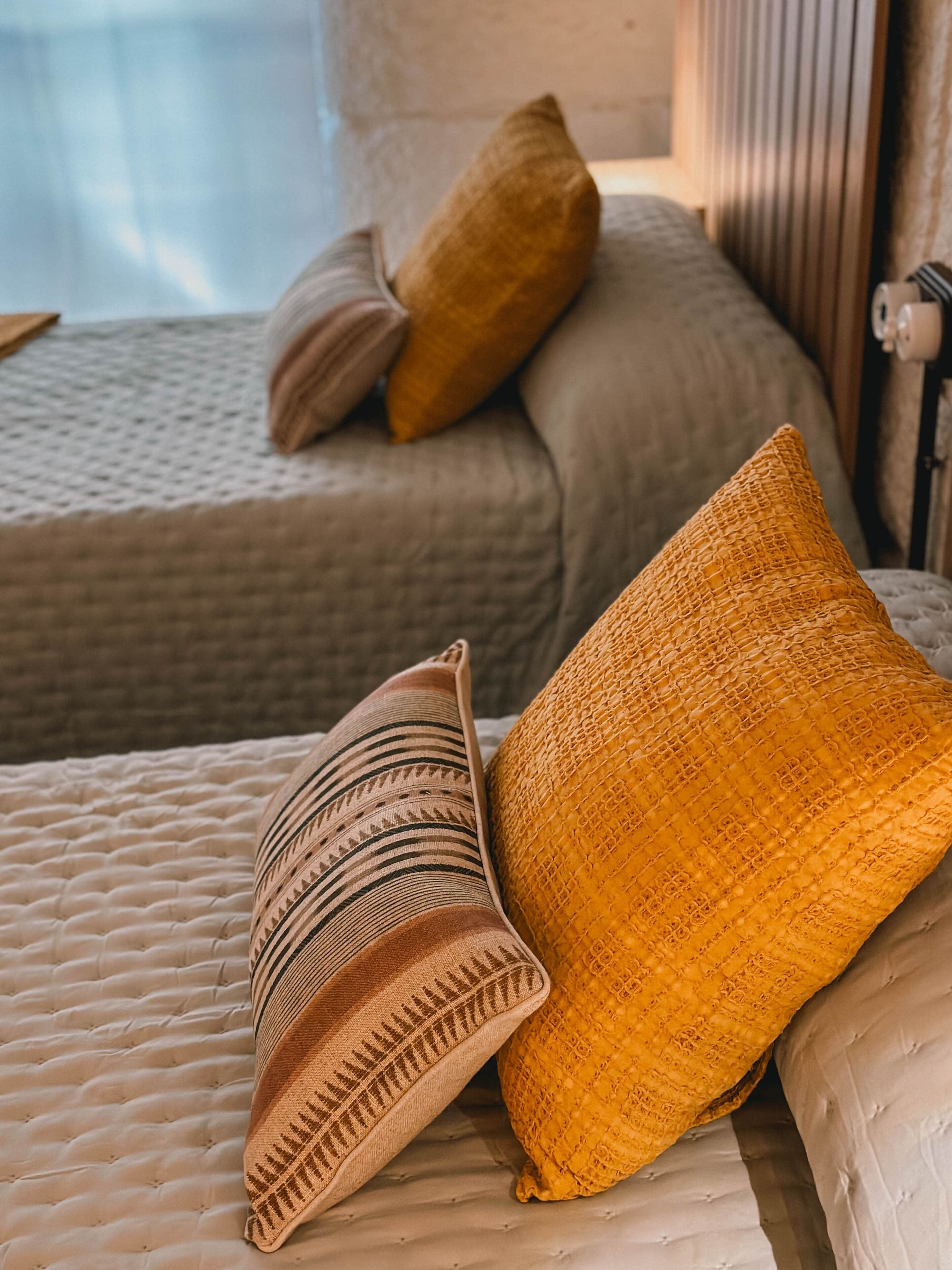 A bed with a textured mattress, two pillows, and a bedside table with a lamp.