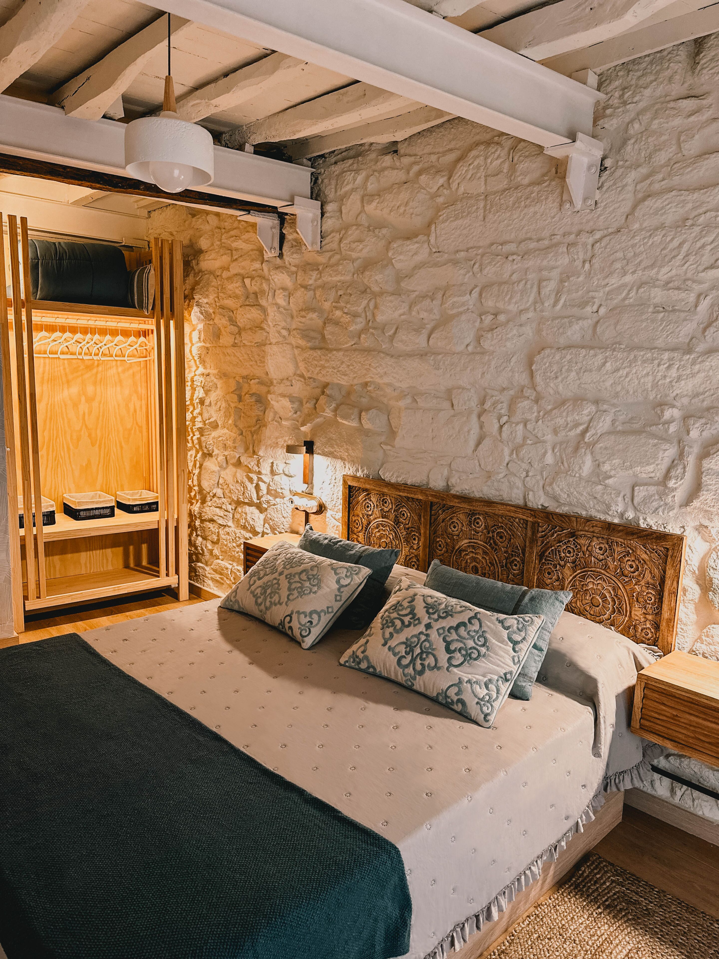 Un dormitorio con pared de piedra, cabecera de madera y cama con ropa de cama estampada.
