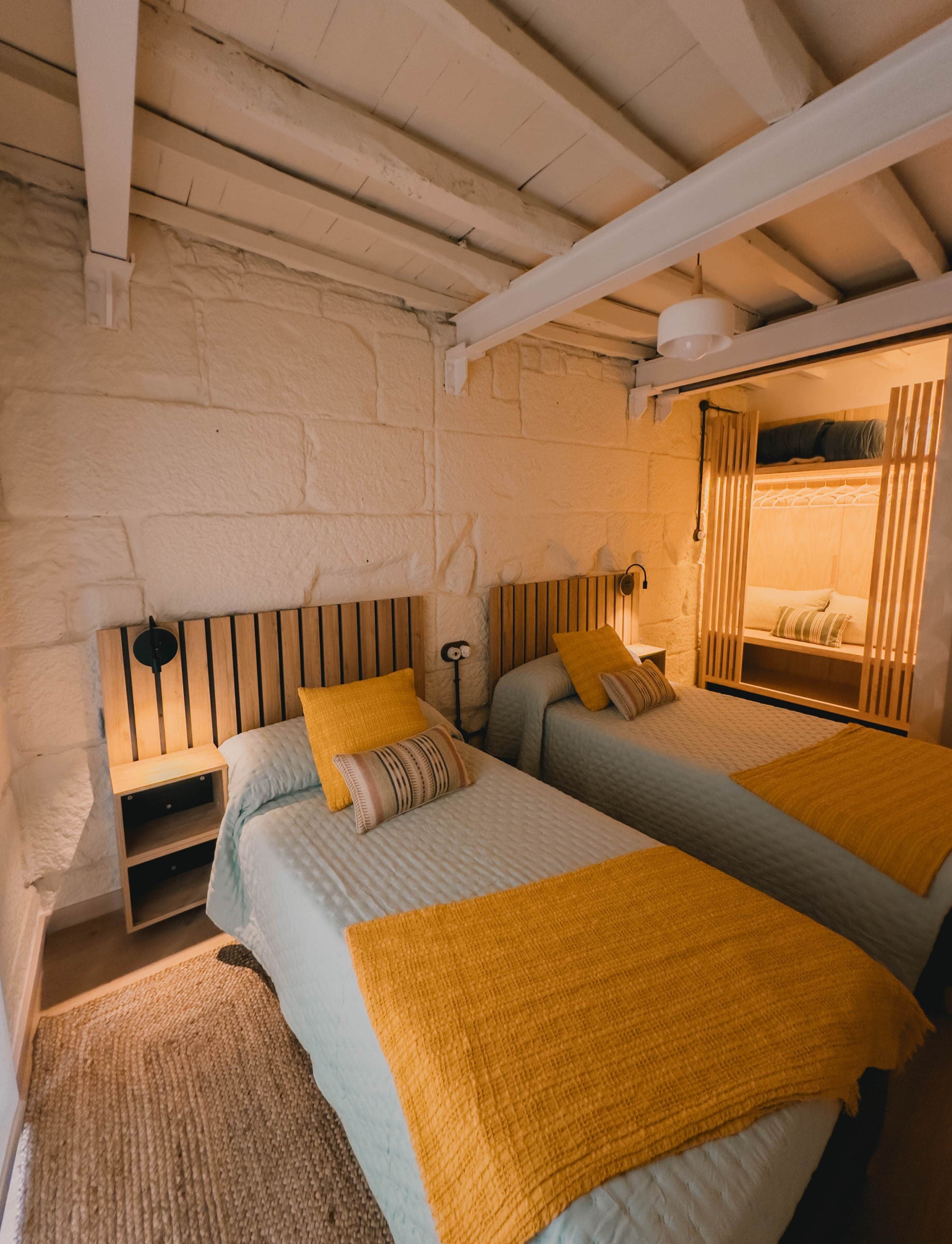 Une chambre avec deux lits, des têtes de lit en bois, une petite table de chevet en bois et une lampe fixée au mur.